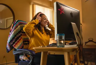 A young woman with headphones on looking at her computer monitor and smiling.