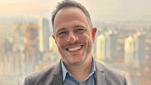Travis Goodman smiling with a city view behind him.